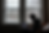 Person in hoodie types on a laptop near large windows on a snowy day. Orange couch and cup nearby, creating a cozy, focused mood.