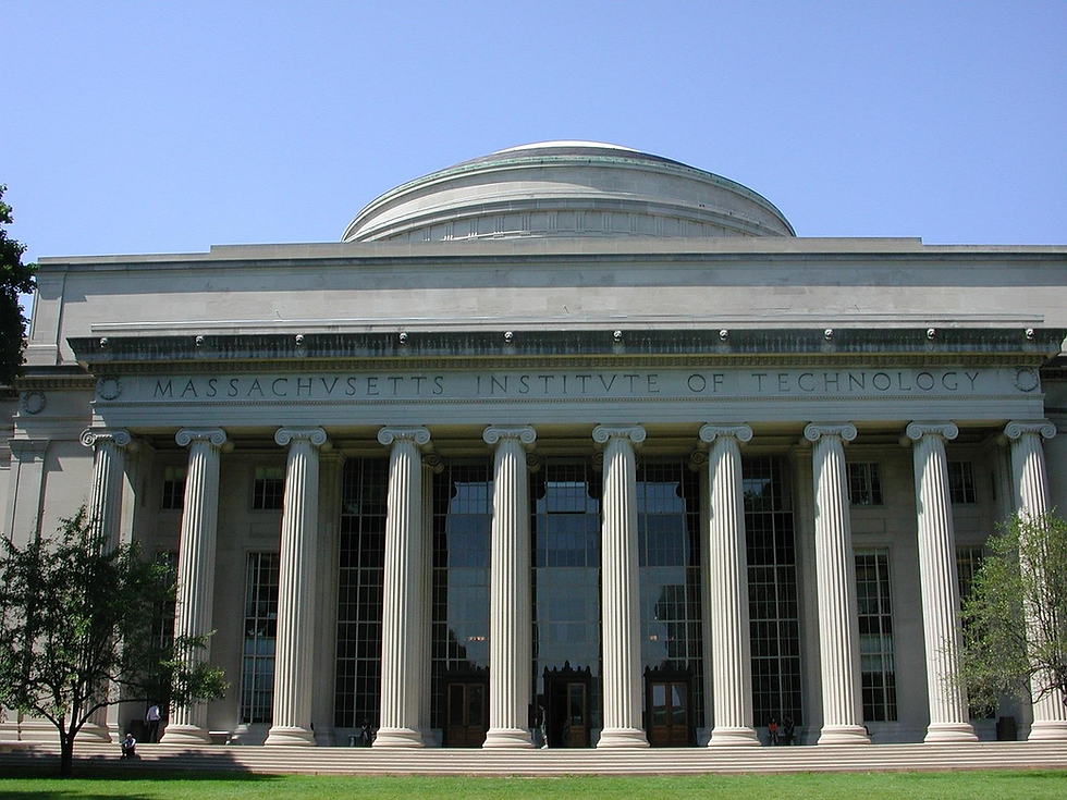 Grand neoclassical building with columns, labeled "Massachusetts Institute of Technology." Sunny day, with a clear blue sky and green lawn.
