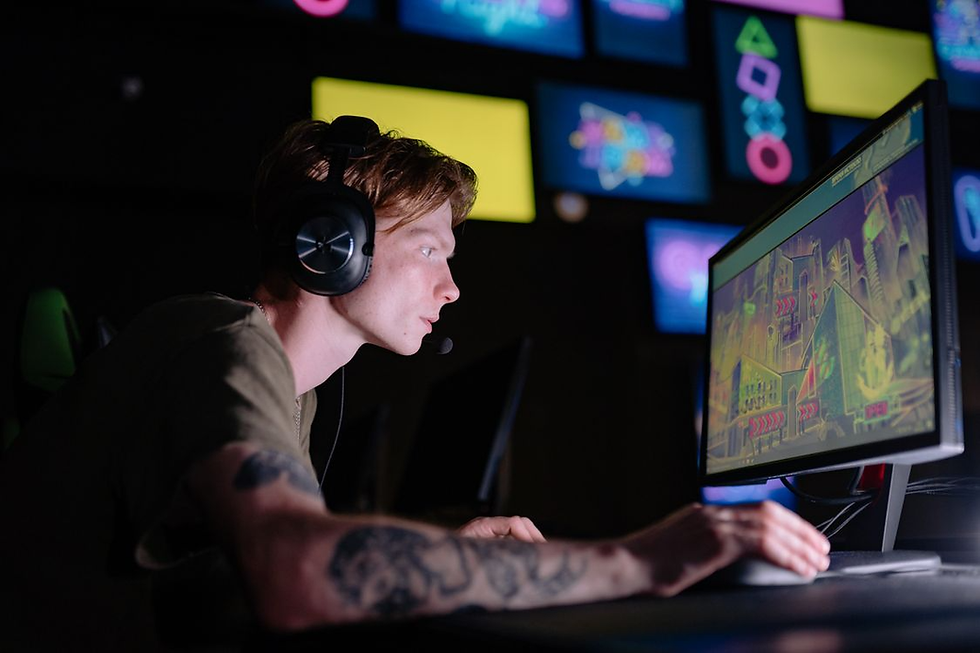 Young gamer in a headset playing at a desktop PC, focused on a neon-lit game screen with colorful monitors behind him.