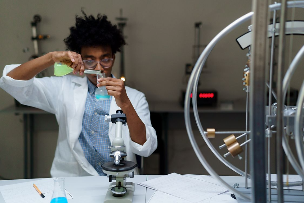Scientist in white lab coat pours green liquid into a beaker beside a microscope in a lab, focused and working carefully.