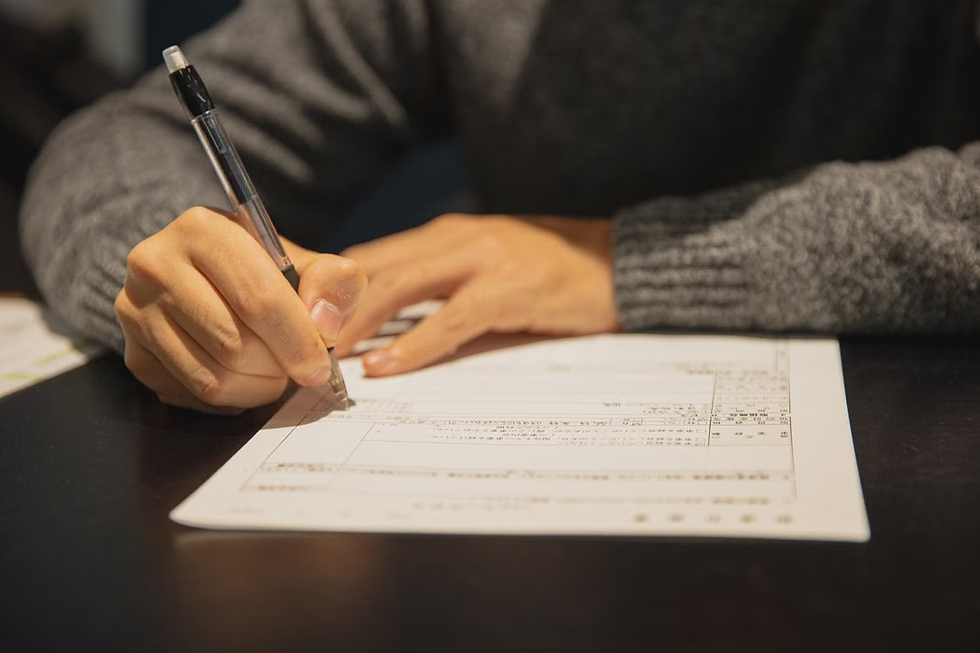 Close-up of hands in a gray sweater filling out a form with a pen on a dark table, focused and quiet.