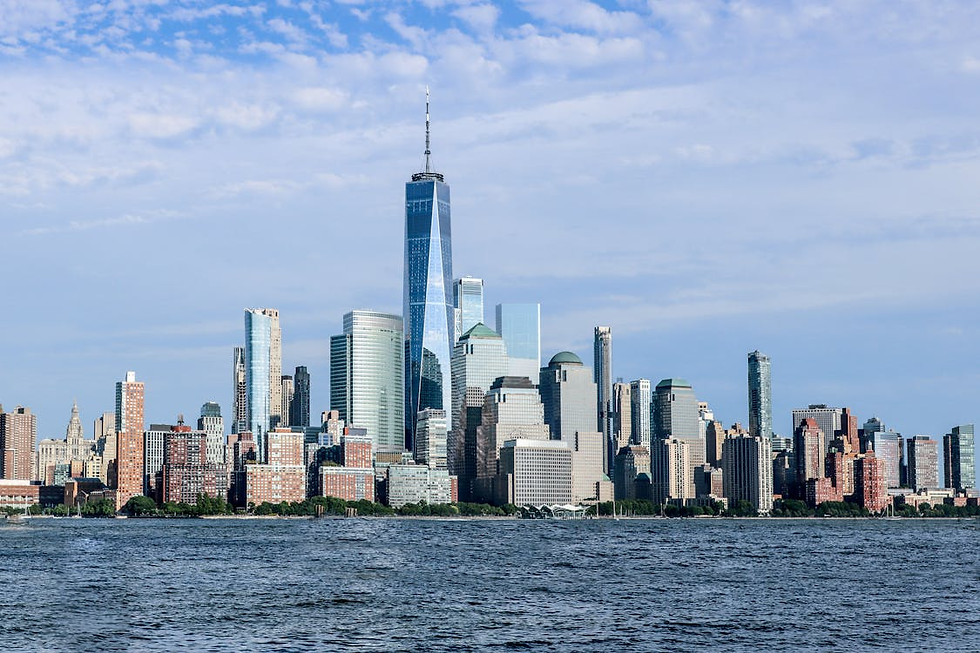 Skyline with tall skyscrapers reflecting sunlight, set against a blue sky. Calm water in the foreground, creating a serene cityscape.