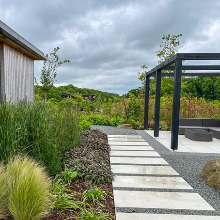 Modern garden with a black pergola, grey seating, and stone path.