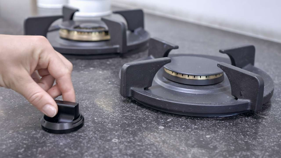 Hand adjusting a black stove knob on a speckled countertop, with two unlit burners in the background. Gray surface, clean setting.
