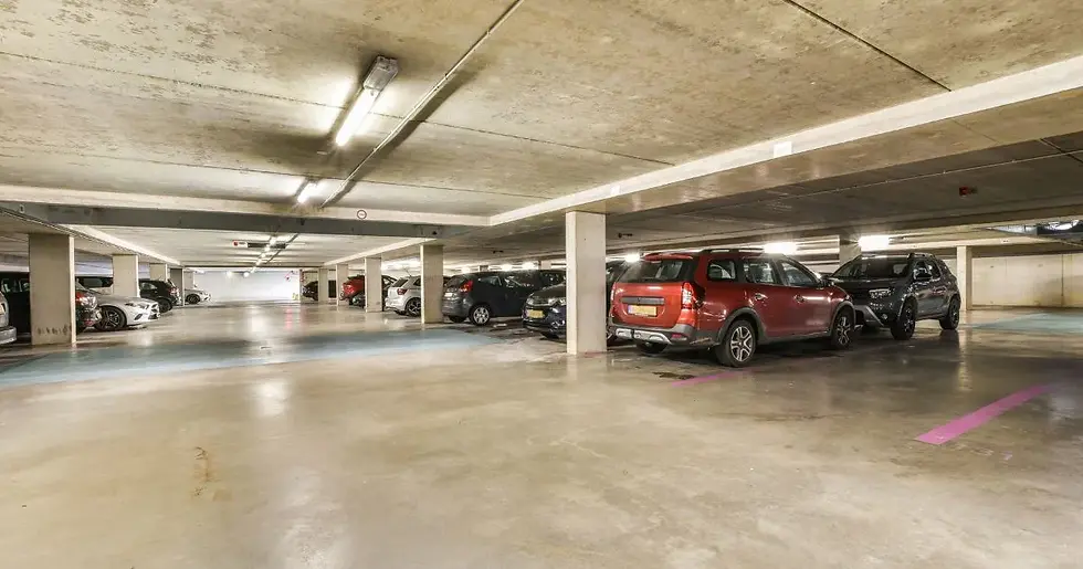 Empty underground parking garage with parked cars, concrete pillars, and fluorescent lighting
