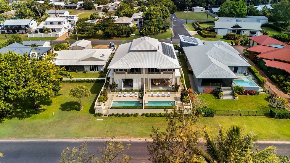 Aerial view of upscale suburban homes with a central house, twin pools, solar panels, and lush green lawns on a quiet street.