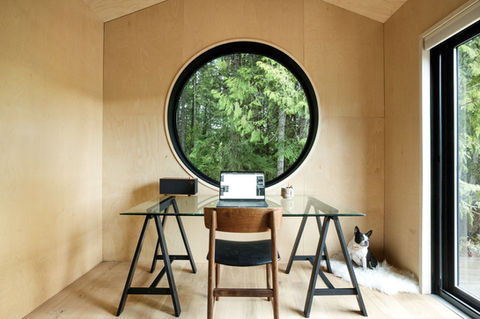 A horitzonal photograph of Woodlot Studio with a round window, a desk and chair in the middle and a dog on the right