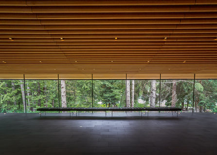 Interior space with only horizontal lines, wood ceiling, long windows looking out into nature with a line of seats with tile 