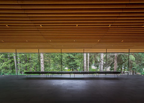 Interior space with only horizontal lines, wood ceiling, long windows looking out into nature with a line of seats with tile 