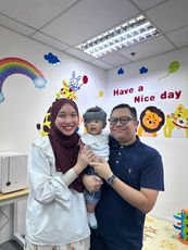 Ibu bapa bersama bayi yang memakai helmet kranial semasa konsultasi terapi helmet pediatrik.