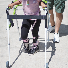 Child walking outdoors using a pediatric mobility walker for rehabilitation support.