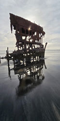 Photo of the Peter Iredale at sunse with the reflections in the shallow tide. 