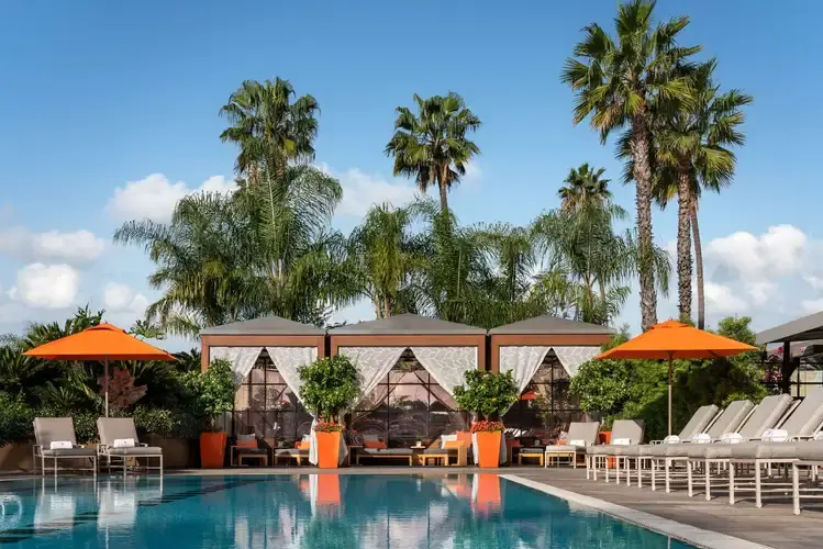 Rooftop swimming pool at Four Seasons Los Angeles surrounded by vibrant, colorful cabanas, patio umbrellas, and palm trees.