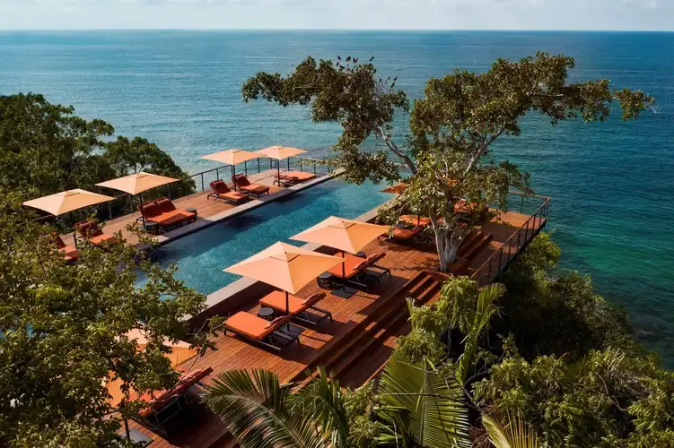 Luxury infinity pool surrounded by lush tropical rainforest canopy with sweeping views of the Pacific Ocean in the background.