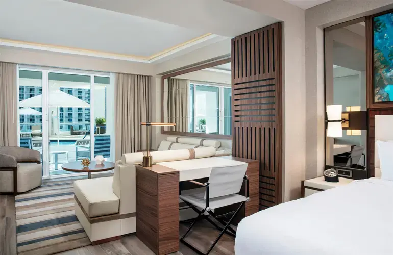 Modern guest room interior at Conrad Fort Lauderdale Beach featuring a comfortable king bed, contemporary coastal furnishings, floor-to-ceiling windows, and a private balcony overlooking the ocean.