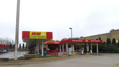 Express tunnel car wash entrance canopy with dual payment kiosks and vacuum stalls on a paved lot.