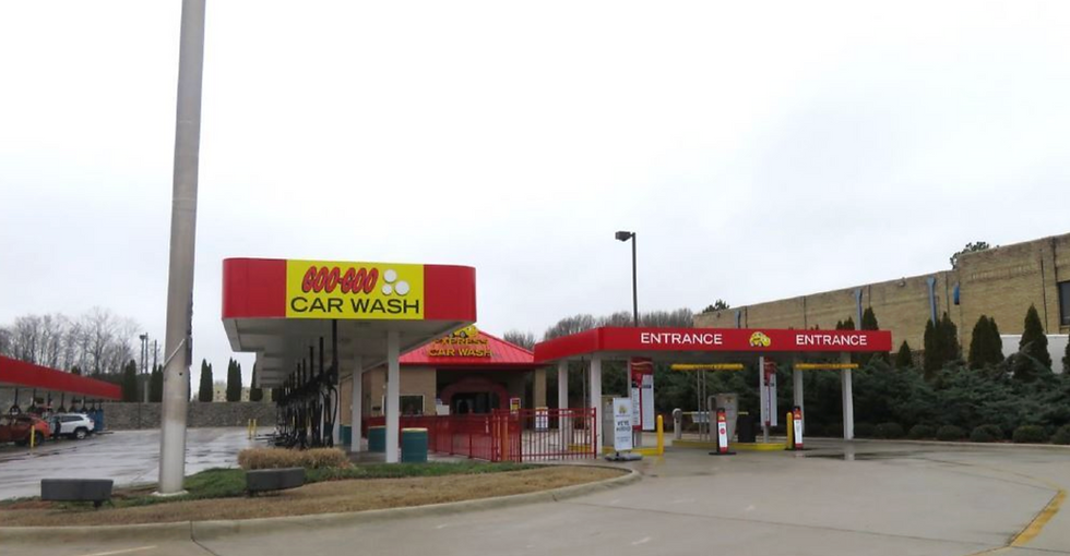 Express tunnel car wash entrance canopy with dual payment kiosks and vacuum stalls on a paved lot.