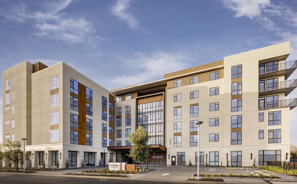 A five-story contemporary multifamily housing development featuring cream stucco and corten steel accent panels, representative of the higher-density residential infill projects emerging from accessory dwelling unit legislation and single-family zoning preemption reform across the United States.