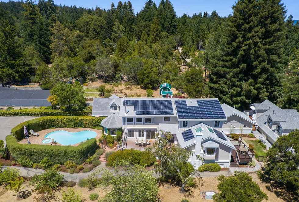 Aerial view of an entitled RV resort clubhouse with solar panels, pool, and landscaped amenities surrounded by forested land — illustrating resort-quality outdoor hospitality development.