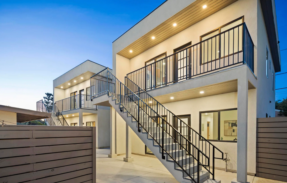 Modern two-story multifamily building with exterior staircase, balconies, and wood privacy fencing at twilight.