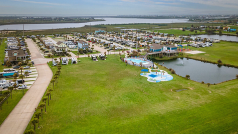 Aerial view of a large waterfront RV resort with high site occupancy, paved pull-through sites, palm-lined roads, pool amenities, and lagoon frontage, illustrating strong demand and upscale infrastructure in the 2025 RV park investment market.