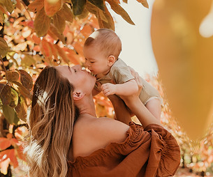 Close up of a mother kissing her baby in the air with colourful autumn leaves