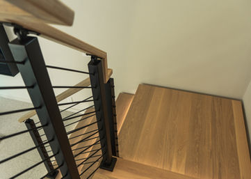 Looking down an oak staircase with wood handrail and stainless cable railing