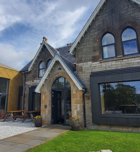 Distillery building with modern glass facade and traditional stone architecture, barrels outside barrels.
