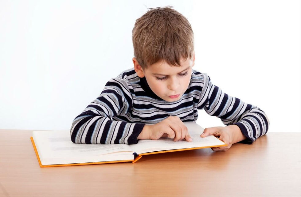 Young boy in striped sweater reading intently at a table. Book with orange cover. White background, focused and studious expression.