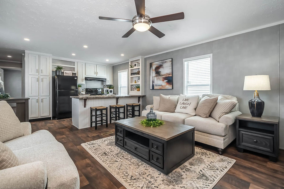 Full kitchen in a manufactured home with brown-speckled granite counters, floor-to-ceiling storage, black refrigerator, matching stove, and stainless steel sink island with three stools.