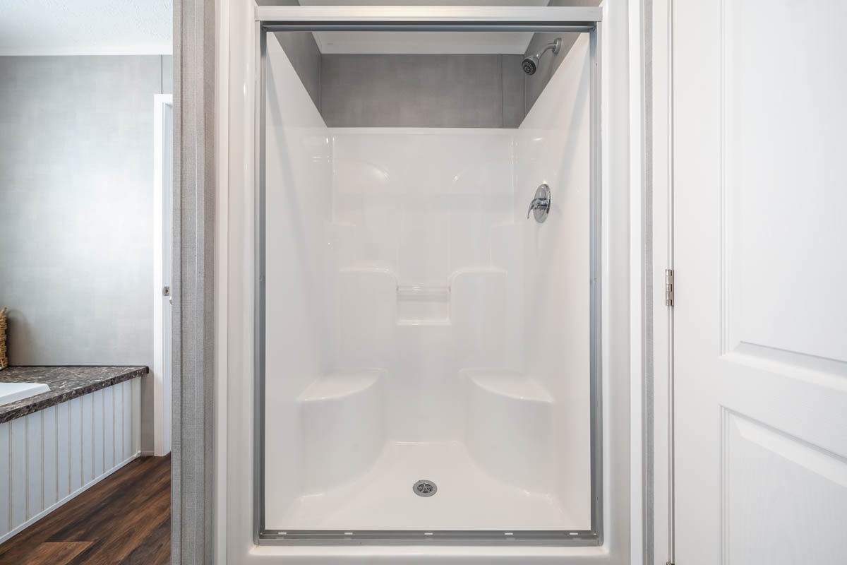 Tall master bathroom shower in a manufactured home with white walls, built-in benches, and chrome fixtures.
