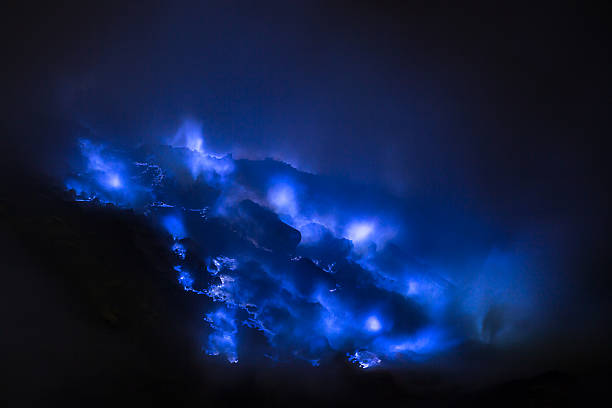 Blue flames light up rocks at night, creating a mysterious and enchanting scene against a dark background with smoke.