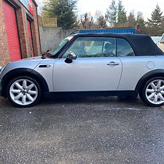 Silver Mini Cooper convertible parked outside building, wet ground.