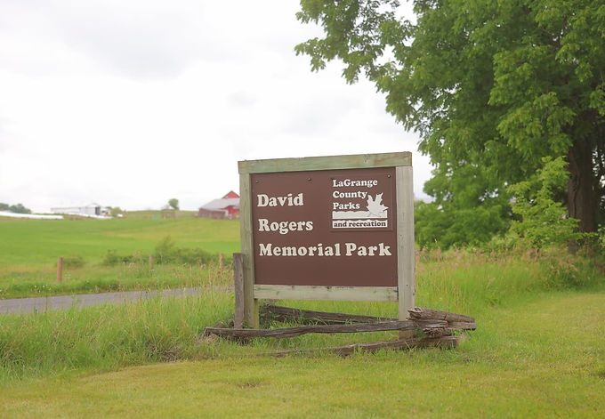 Wide view of David Rogers Memorial Park with wood buildings and green trees.