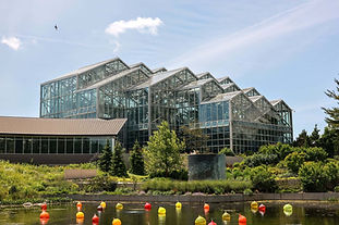 Glass conservatory at Frederik Meijer Gardens & Sculpture Park in Grand Rapids, Michigan, viewed across a pond with colorful glass sculptures.