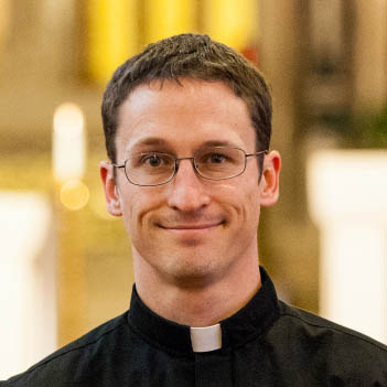 Monsignor Bernie Schmidt gives a blessing at the altar, surrounded by candles and a gathering.