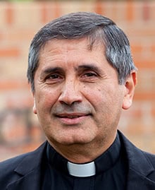 Monsignor Bernie Schmidt gives a blessing at the altar, surrounded by candles and a gathering.