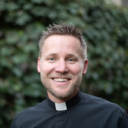 Monsignor Bernie Schmidt gives a blessing at the altar, surrounded by candles and a gathering.