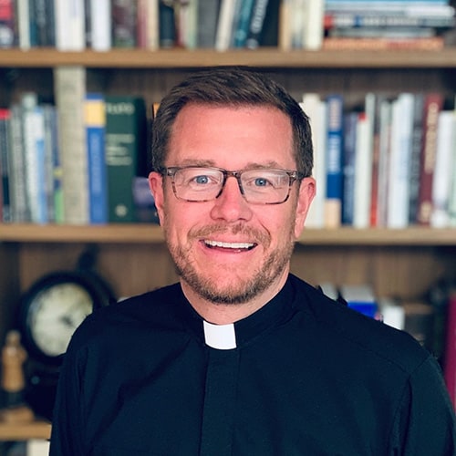 Monsignor Bernie Schmidt gives a blessing at the altar, surrounded by candles and a gathering.