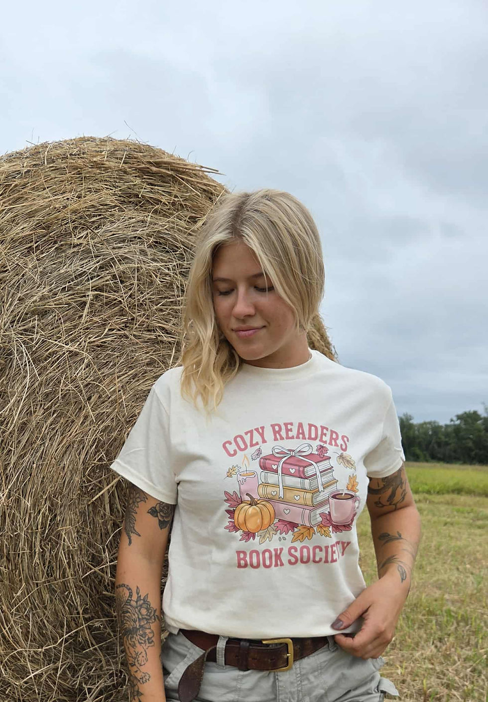 Thumbnail: Woman wearing 'Cozy Readers Book Society' t-shirt next to hay bale