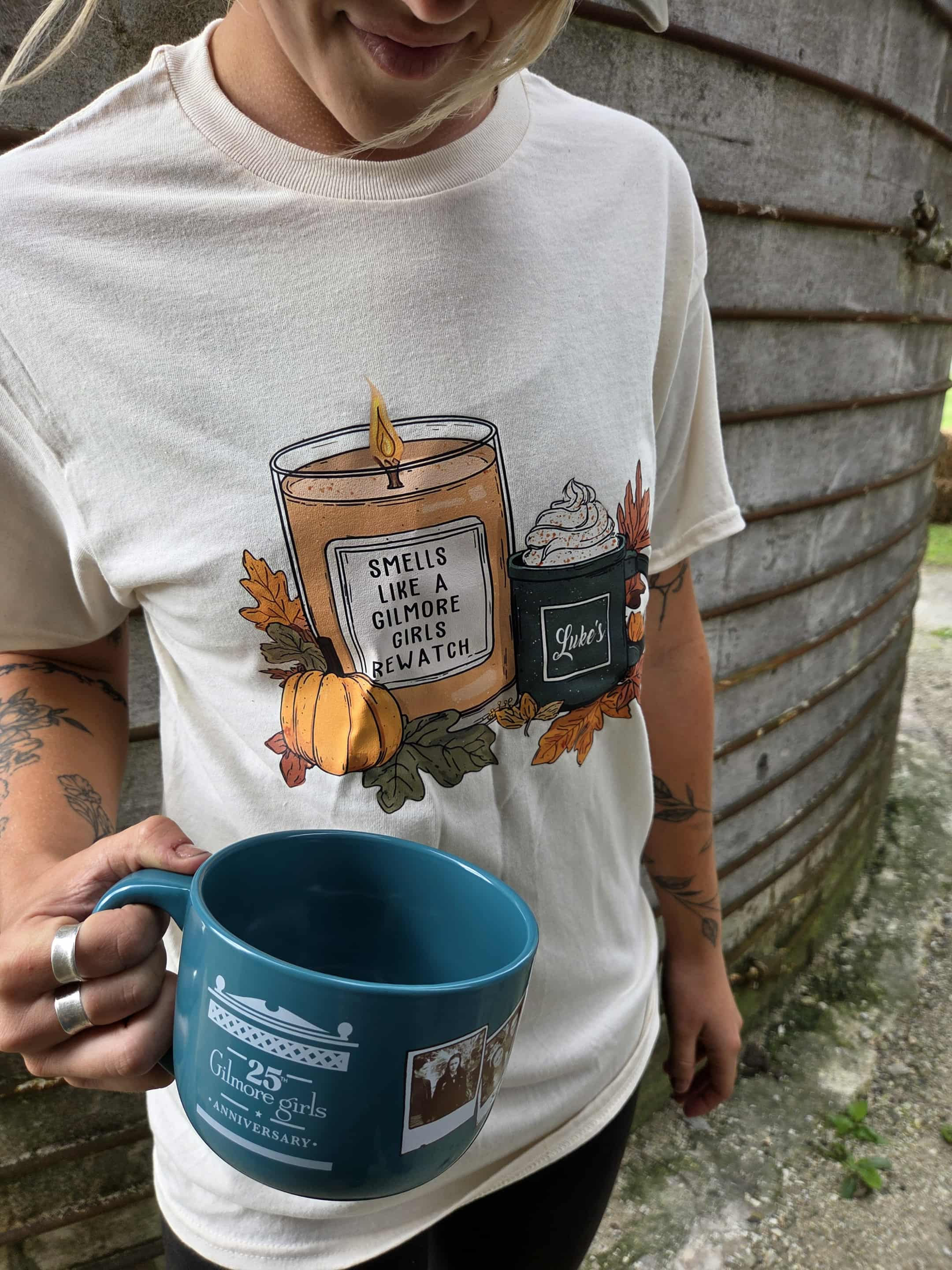 Person wearing 'Smells Like a Bookstore' candle t-shirt, holding a blue mug.