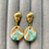 Thumbnail: Shimmery white, brown and teal drop earrings on gold plated sea shell studs