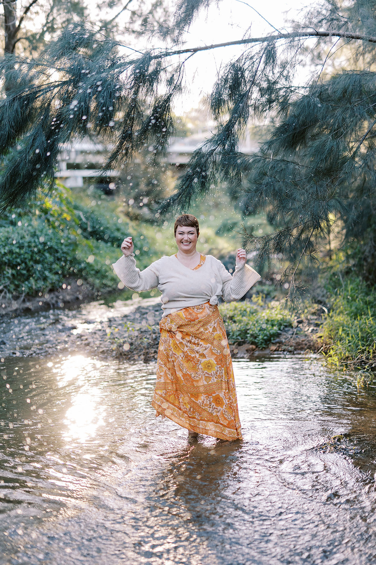 woman smiling standing in a beautiful creek with the light on her back for website photography