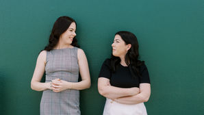 two business women standing against a green wall looking at each other during a headshot photoshoot