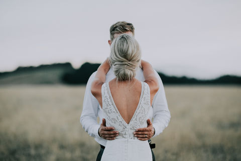 A bride and groom embrace at sunset in a paddock at Cape Kidnappers in Hawkes Bay