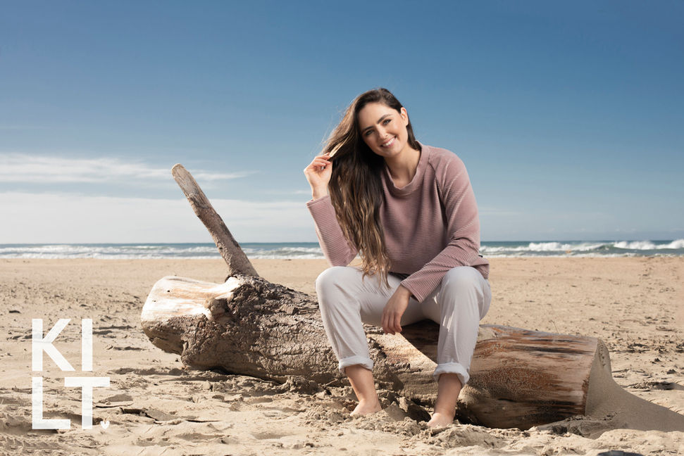 A brunette model wearing pink sitting on a log at Hawke's Bay's Ocean Beach for a fashion photography shoot