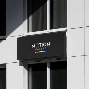 Letrero negro con logotipo de Motion Makers y barra de color sobre fachada blanca.