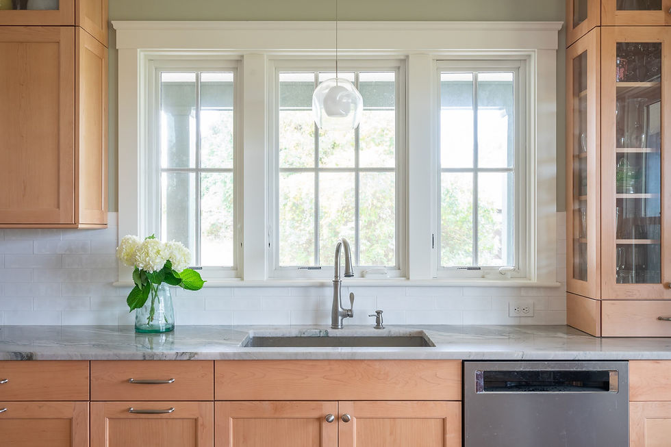 Kitchen with natural wood cabinets, glass-front pantry, stone countertops, stainless steel dishwasher, and large windows letting in natural light.