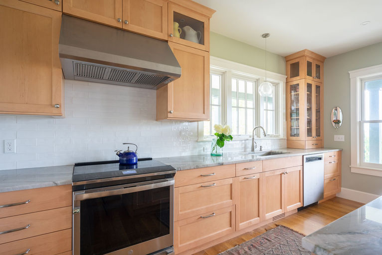 Bright kitchen with natural wood cabinets, stainless steel range, white subway tile, and a large central island with a thick, veined marble countertop. Designed by Apex Kitchens and Baths in Middletown Rhode Island
