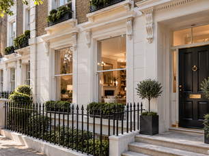 Period London townhouse with white stucco detailing, tall sash windows, black iron railings and a black front door with brass fittings.